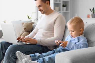 Oğlu evde cep telefonuyla oynarken babası çalışıyor.