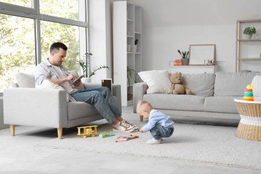 Oğlu cep telefonuyla oynarken babası tabletle çalışıyor.