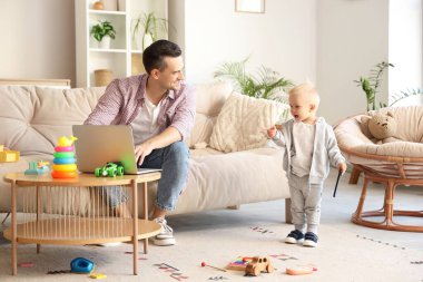 Küçük oğlu ve dizüstü bilgisayarı evde olan genç bir baba.