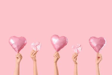 Kalp şeklinde balonlar tutan kadın eller ve pembe arka planda hediye kutuları. Sevgililer Günü kutlaması
