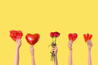 Kalp şeklinde balonu olan kadın elleri, hediye kutuları, çikolata kalıpları ve sarı arka planda kırmızı güller. Sevgililer Günü kutlaması