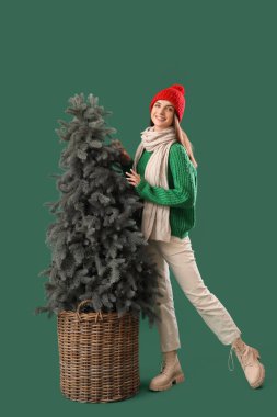 Yeşil arka planda, Noel ağacının yanında şık, sıcak giysiler içinde güzel genç bir kadın.