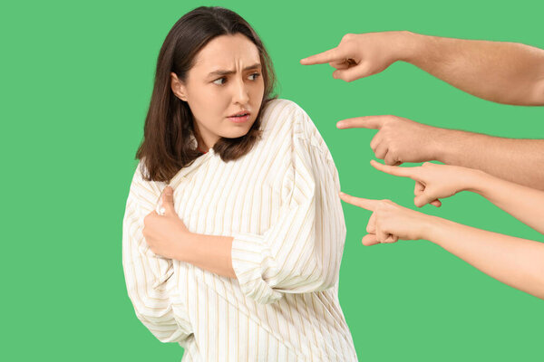People pointing at scared young woman on green background. Accusation concept