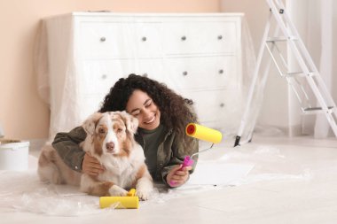 Yeni evdeki tamirat sırasında sevimli Avustralyalı çoban köpeği ve bigudili mutlu Afro-Amerikan ressam.