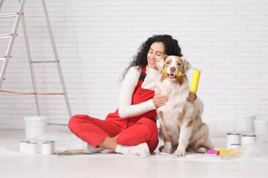 Mutlu Afro-Amerikan ressam üniformalı, patenli ve şirin Avustralyalı çoban köpeği evde tamir sırasında oturuyor.