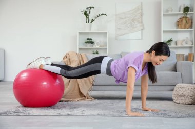 Sportif genç bayan evde spor topuyla egzersiz yapıyor.