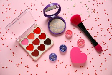Parıltı kavanozları, konfeti, makyaj ürünleri ve pembe arka planda fırçayla kompozisyon