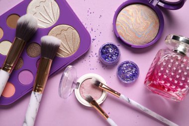 Parfüm şişesi, sim kavanozu, makyaj ürünleri ve leylak arkaplanda fırçalar.