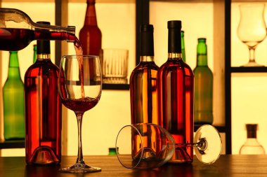 Barda şişeler olan rafların yanındaki bardaklara kırmızı şarap dökülüyor.