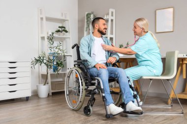 Steteskoplu kadın doktor hastanede tekerlekli sandalyedeki genç adamı dinliyor.