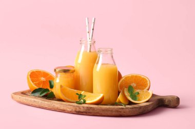 Naneli taze portakal suyu şişeleri ve pembe arka planda meyveler.