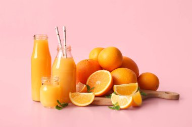 Naneli taze portakal suyu şişeleri ve pembe arka planda meyveler.