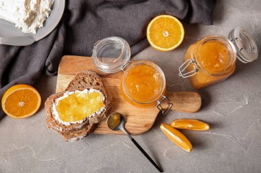 Tahta tahta tahta, ekmek dilimleri ve gri arka planda bir kavanoz tatlı portakal reçeli.
