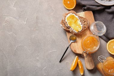 Tahta tahta tahta, ekmek dilimleri ve gri arka planda bir kavanoz tatlı portakal reçeli.