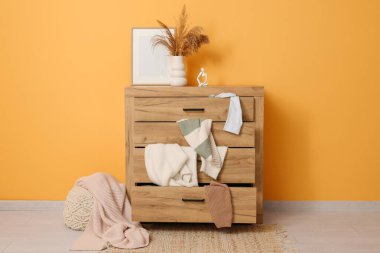 Oturma odasındaki sarı duvarın yanında dağınık giysilerle tuvalet.