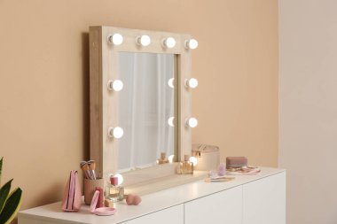 Parlayan ayna ve bej duvarın yanında makyaj malzemeleri olan giyinme masası.