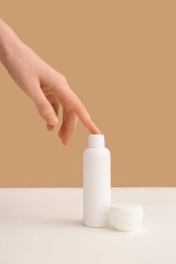 Bej arka planda şişe ve kozmetik ürünlerle dolu bir kadın eli.