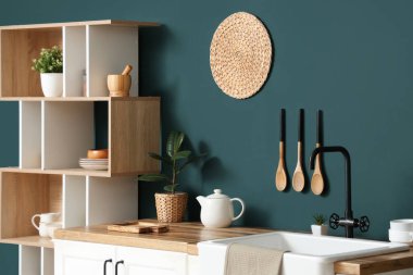 Mutfağın içinde raf ünitesi ve mavi duvarın yanındaki masa.