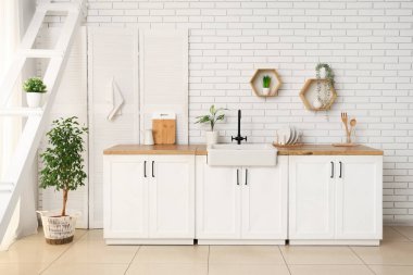 Beyaz tuğla duvarın yanında tezgah ve katlanır ekran olan mutfağın içi