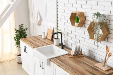 Mutfaktaki beyaz tuğla duvarın yanında lavabo ve çiçek tezgahları var.