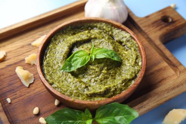 Ahşap tahta tahtada bir kase lezzetli pesto sosu ve mavi arka planda malzemeler.