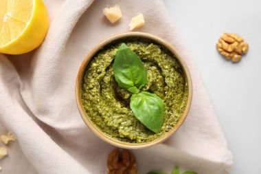 Beyaz arka planda ceviz, peynir ve fesleğen yapraklı bir kase lezzetli pesto sosu