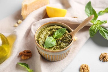 Beyaz arka planda ahşap kaşık, ceviz ve fesleğen yapraklı lezzetli pesto sosu.