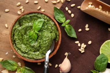 Bir kase lezzetli pesto sosu, kaşık ve ahşap arka planda malzemeler.