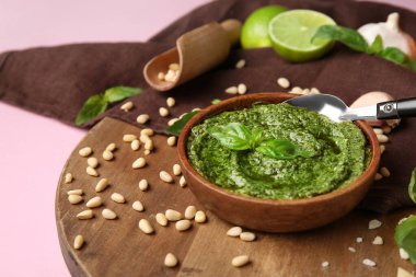 Ahşap tahta tahtada lezzetli pesto sosu, kaşık ve pembe arka planda malzemeler var.