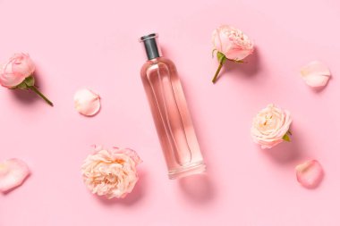 Bir şişe parfüm ve pembe arka planda güzel güller.
