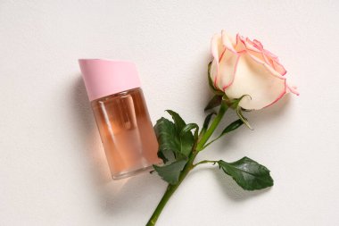 Bir şişe parfüm ve beyaz arka planda güzel bir gül.
