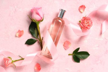 Açık pembe arka planda güzel güller ve taç yapraklarıyla bir şişe parfüm.