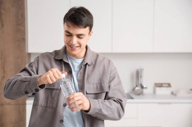 Yakışıklı genç adam evde bir şişe su açıyor.