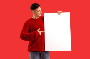 Yakışıklı genç adam kırmızı arkaplanda boş posterlere bakıyor.