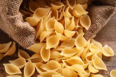 Ahşap arka planda çiğ makarna kabukları olan çanta, yakın plan.