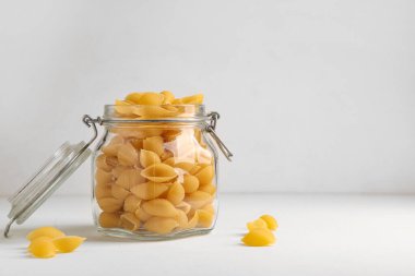 Beyaz arkaplanda çiğ makarna kabukları olan kavanoz.