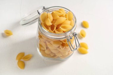 Beyaz arkaplanda çiğ makarna kabukları olan kavanoz.