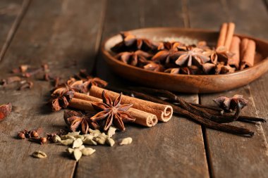 Tahta zemin üzerinde anason yıldızları, tohumlar, tarçın ve vanilya çubukları olan tabaklar.