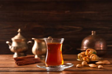 Tahta zemin üzerinde tarçın çubukları ve bademlerle bir bardak Türk çayı.