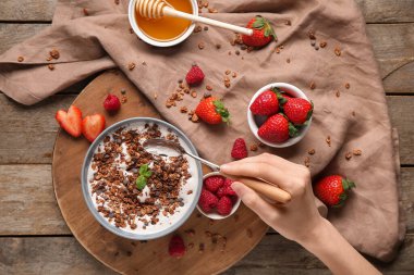 Bir kase çikolatalı mısır gevreği, yoğurt ve ahşap arka planda böğürtlen taşıyan kadın eli.