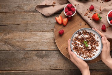 Bir kase çikolatalı mısır gevreği, yoğurt ve ahşap arka planda böğürtlen taşıyan kadın elleri.