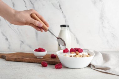 Bir kase mısır gevreği, yoğurt ve mermer arka planda böğürtlen taşıyan bir kadın eli.