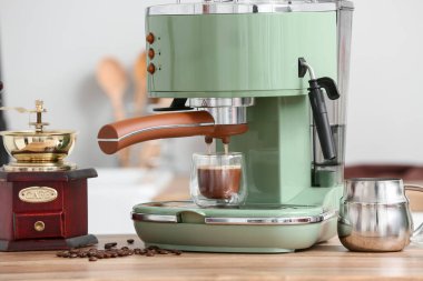 Mutfaktaki ahşap masada bir bardak sıcak espresso ve fasulye ile modern kahve makinesi.