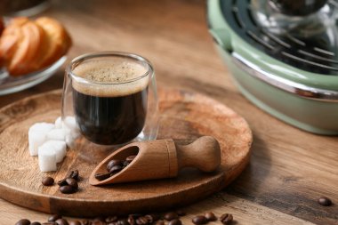 Bir bardak sıcak espresso, fasulye ve ahşap arka planda modern kahve makinesi.