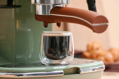 Bej arka planda bir bardak sıcak espresso ile modern kahve makinesi, yakın plan.