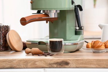 Modern kahve makinesi, bir bardak sıcak espresso ve mutfaktaki ahşap masada tatlı kekler.