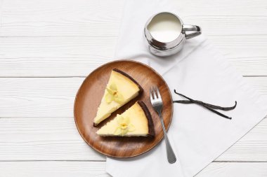 Beyaz ahşap zemin üzerinde tatlı vanilyalı cheesecake ve sütle dolu bir tabak.