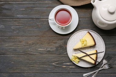 Bir tabak vanilyalı cheesecake ve siyah ahşap zemin üzerinde çay.