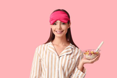 Elinde mısır gevreği halkaları ve pembe arka planda sütle kaseyi tutan genç bir kadın.