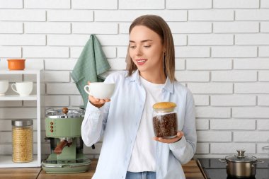 Mutfakta bir fincan sıcak kahve ve bir kavanoz fasulye ile güzel genç bir kadın.